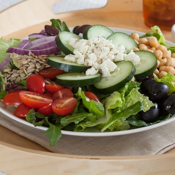 A fresh salad with lettuce, tomatoes, cucumbers, feta, chickpeas, olives, red onion, and sunflower seeds.