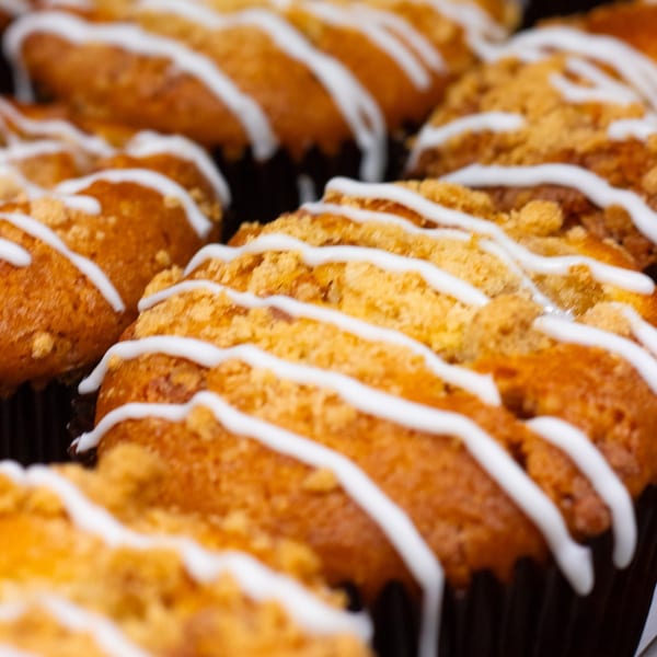 Close-up of Green Beans Coffee muffins with crumb topping and white icing drizzle.