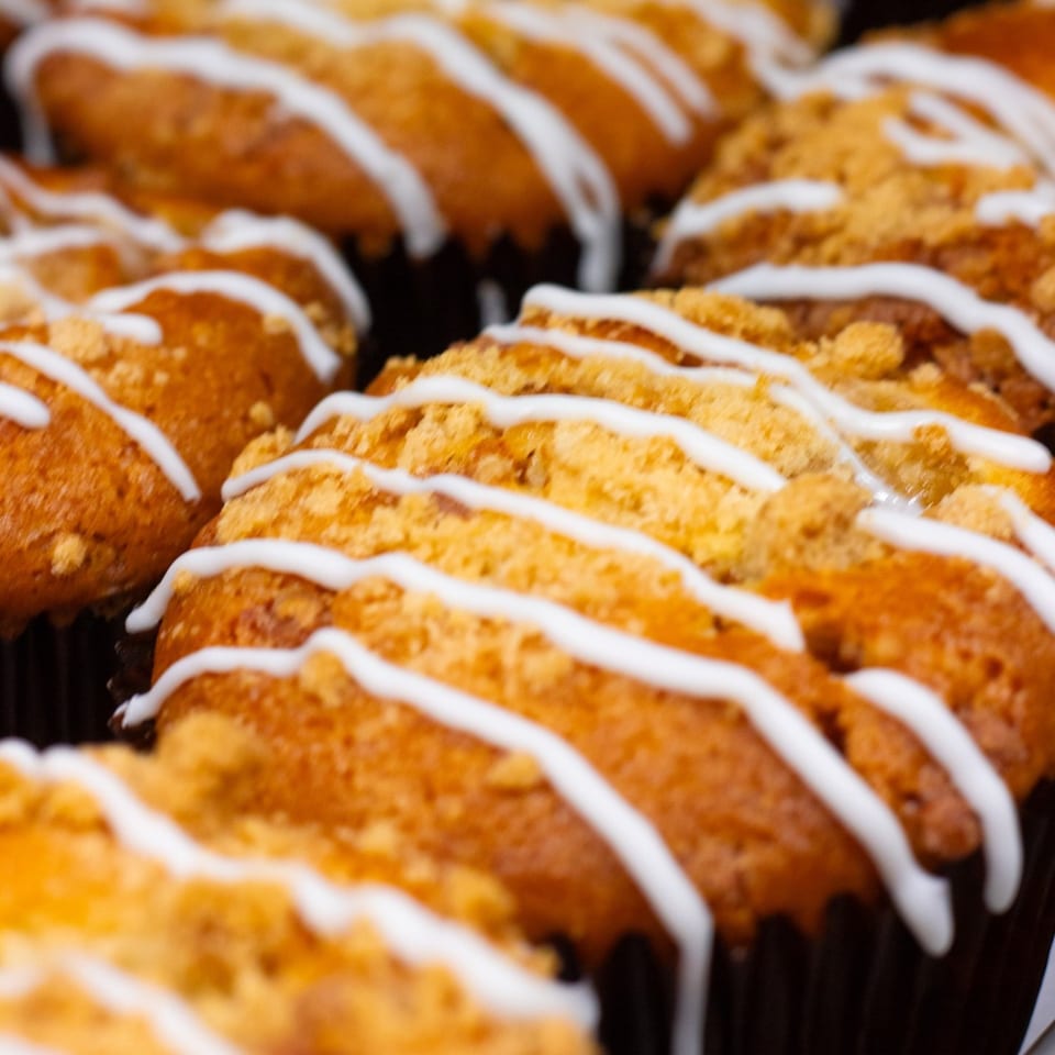 Close-up of Green Beans Coffee muffins with crumb topping and white icing drizzle.