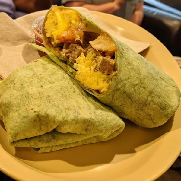 Two Green Beans Coffee breakfast burritos on a yellow plate, one open revealing eggs, potatoes, and meat.